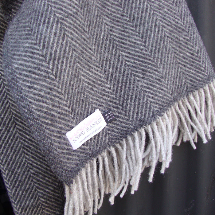 Charcoal and silver herringbone wool blanket with white fringe, visibly showing the Solway Blankets label 