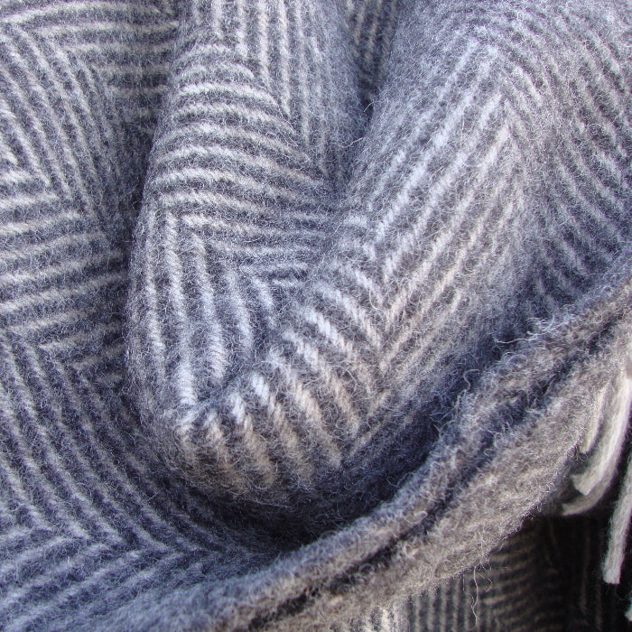 Close-up of a charcoal and silver herringbone patterned wool blanket with fringes.