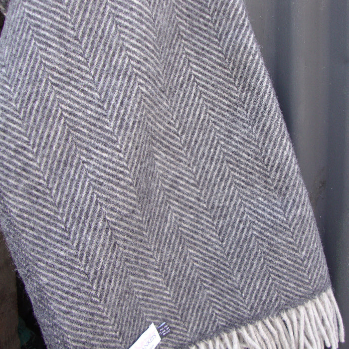 Charcoal and silver herringbone patterned blanket with fringes on a dark background outdoors
