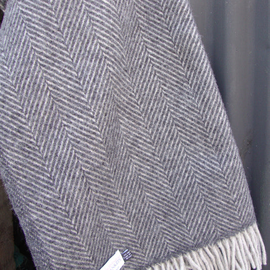 Charcoal and silver herringbone patterned blanket with fringes on a dark background outdoors