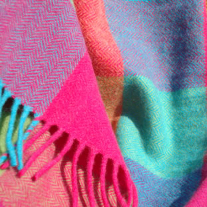 Close up of a colorful lambswool patchwork throw with fringes in pink, blue, and green.