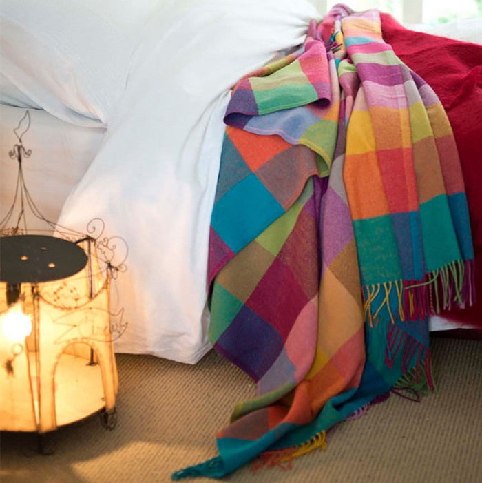 Colorful patchwork patterned throw draped over a bed next to a lamp.