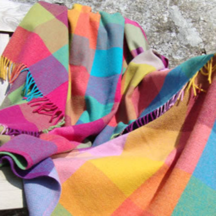 Colorful lambswool patchwork throw with fringe on a wooden surface