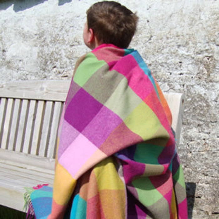 Person sitting on a bench with a colorful lambswool patchwork throw draped over them