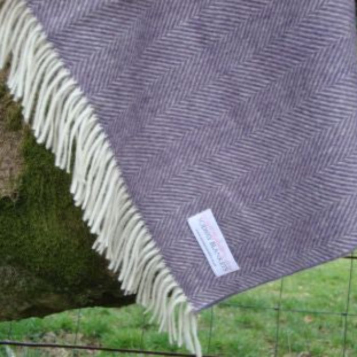 Purple woven herringbone patterned blanket throw with white fringe draped over a tree