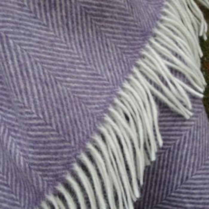 Close up of a purple herringbone patterned blanket throw with white fringes on a green fabric background