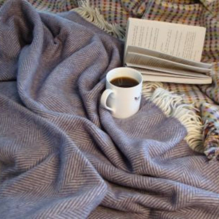 Purple herringbone patterned wool blanket throw placed underneath a cup of coffee and book