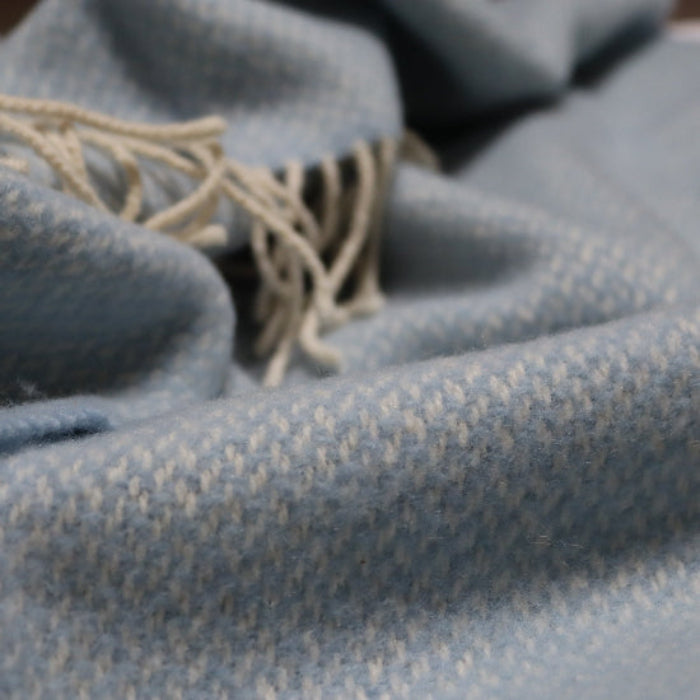 Close-up of the Connor Blue Cashmere Baby Blanket a textured pale blue woven pram blankets with a delicate fringe trim