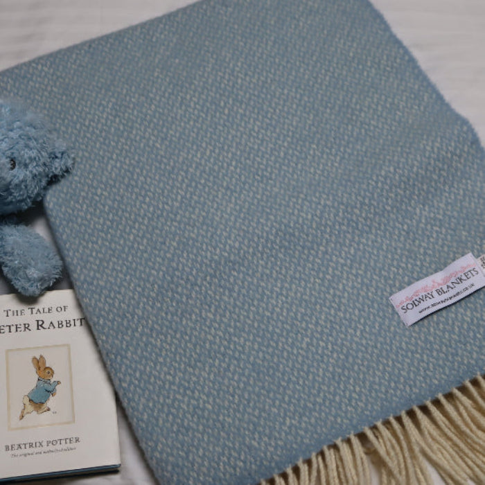 Connor Blue Cashmere Baby Blanket with a Solway Blankets tag, teddy bear, and book on a light background