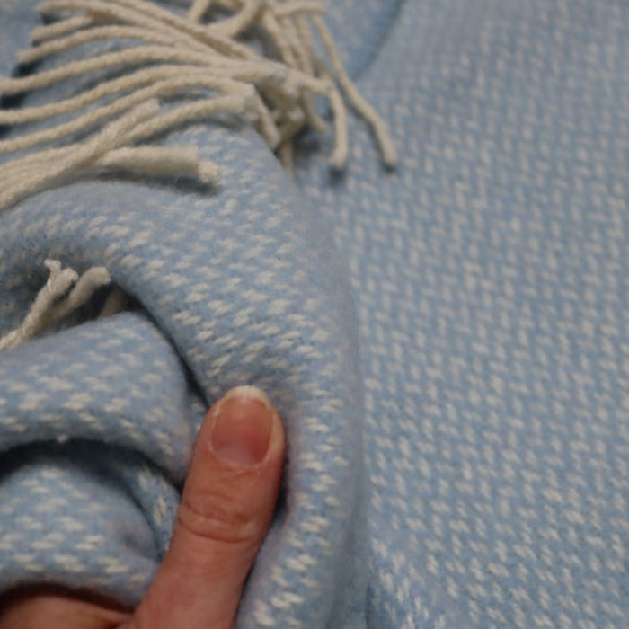 Close-up of a the Connor Blue Cashmere Baby Blanket, textured weave with fringes, held by a hand feeling super softness
