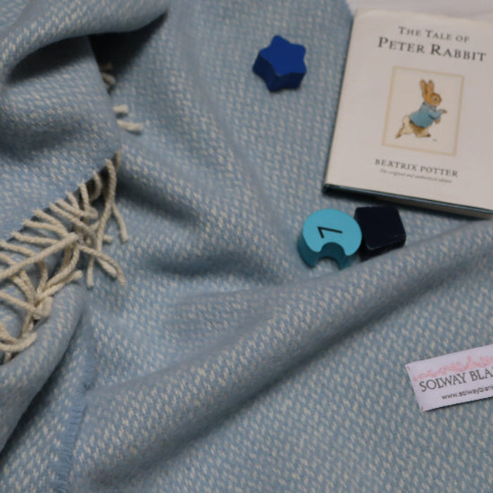 Connor Blue Cashmere Baby Blanket with decorative elements and a book titled 'The Tale of Peter Rabbit' on a white background.