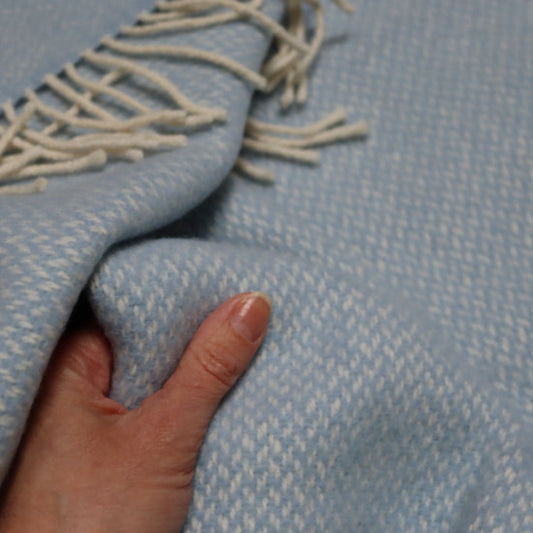 Connor Blue Cashmere Baby Blanket with a hand touching it, feeling softness and texture.
