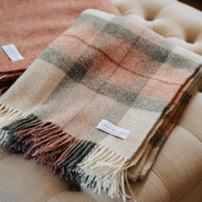 Coral Skye Check Shetland Wool Throw Plaid blanket with fringes on a beige footstool, featuring the Solway Blankets brand label.