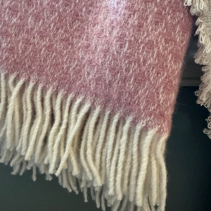 Close up of a textured soft pink wool throw with fringe on a dark background