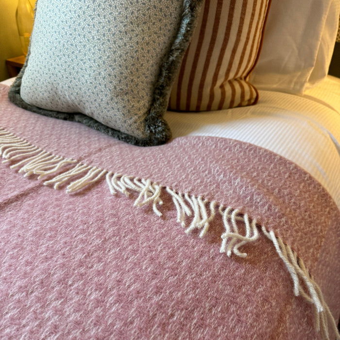 Close up of a soft pink textured throw with fringe on a bed with striped and patterned pillows.