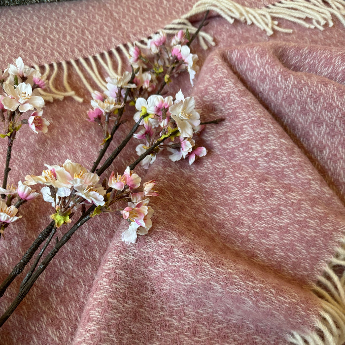 Close up of a textured soft pink wool throw with floral embellishments lain on top 