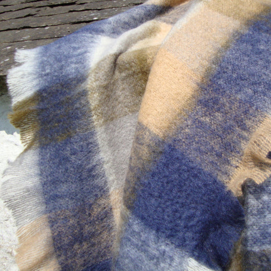 Denim & Stone Mohair Throw with blue and beige colours on a painted stone and slate surface outside with the sun 