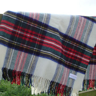 Dress Royal Stewart Tartan Plaid blanket rug with fringes draped over a wooden fence in a grassy field.
