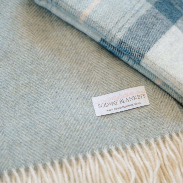 Two blankets, Duck Egg Blue Herringbone Shetland Wool Blanket and Blue Skye Check Throw with a visible 'Solway Blankets' label