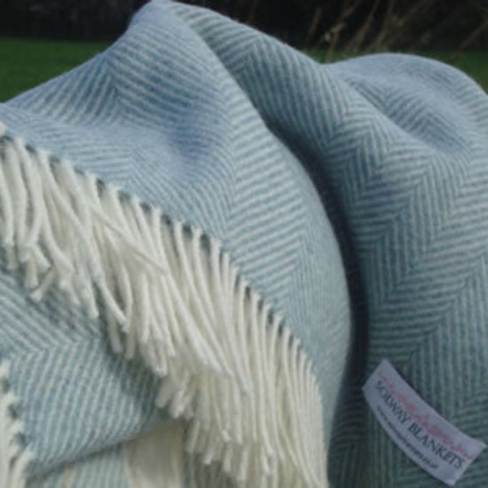 Duck Egg Blue Herringbone Shetland Wool Throw a Light blue woven blanket with white fringe and a visible Solway Blankets brand label.