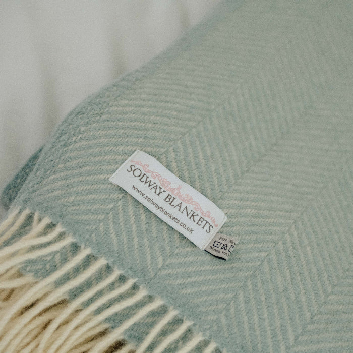 Duck egg coloured woolen blanket in a fishbone style displaying a Solway Blankets label