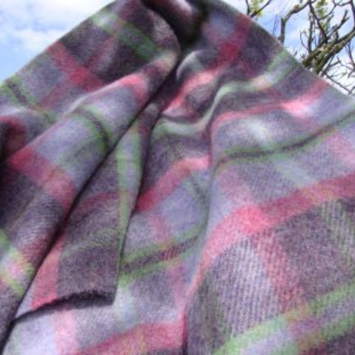 Plaid wool blanket with shades of pink, purple and green colours draped over a tree branch against a blue sky.