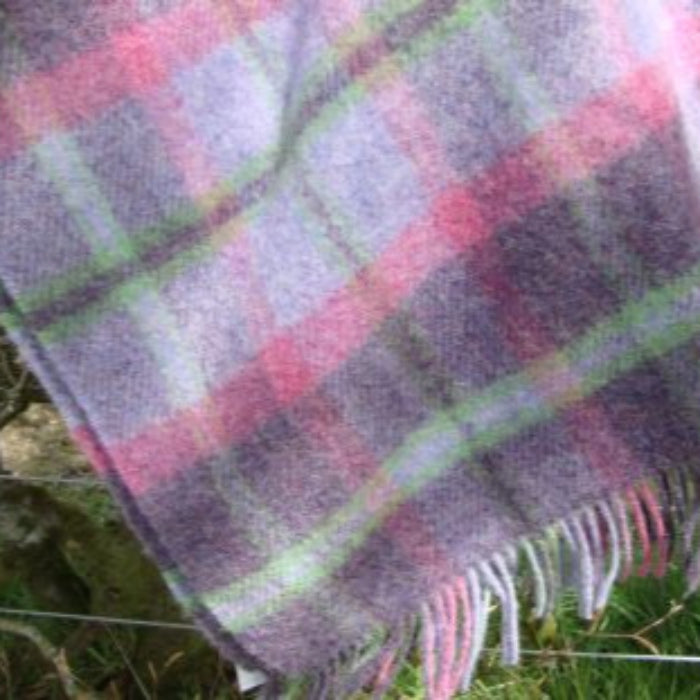 Plaid wool blanket with pink, purple and green pattern draped over a wire fence outdoors