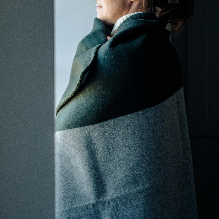Person with a bottle green and grey cashmere blanket throw wrapped around them, standing against a plain background.