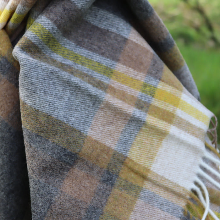Plaid beige, charcoal and yellow lambswool throw with fringes against a blurred natural background