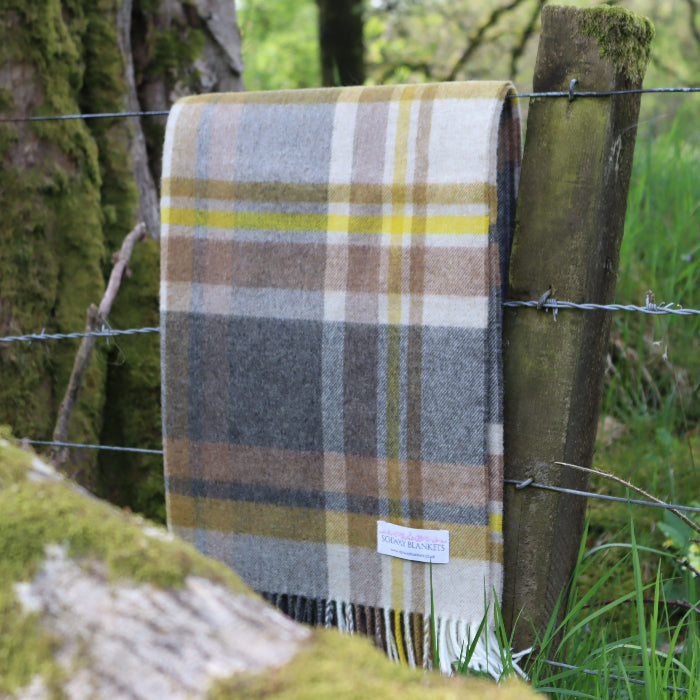 Plaid beige, charcoal and yellow throw draped over a fence with a Solway Blankets label in an outdoor setting