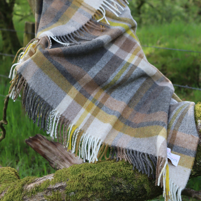 Plaid throw with colours of beige, charcoal and yellow with fringe draped over a tree branch in a natural setting