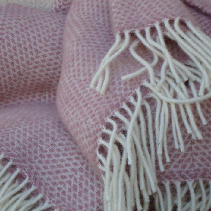 Close up of a dusky pink woven fabric with white fringe on a textured surface