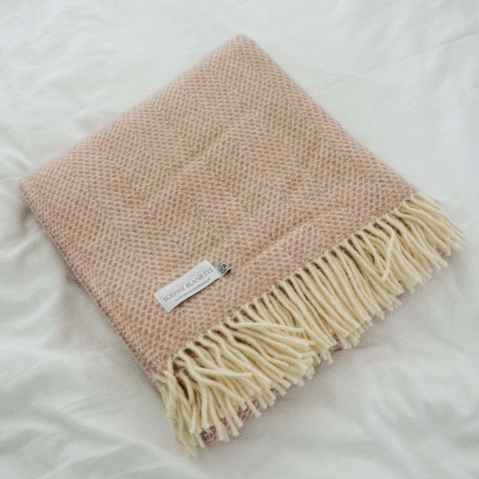 Dusky pink beehive textured wool blanket with fringe on a white bedding surface
