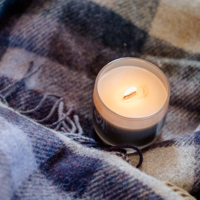 Close up of a plaid wool blanket with fringe, with a lit candle in a jar placed on top