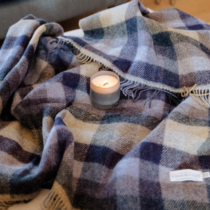 Plaid wool blanket draped over a pouffe with a candle on top, in a cozy living room setting.