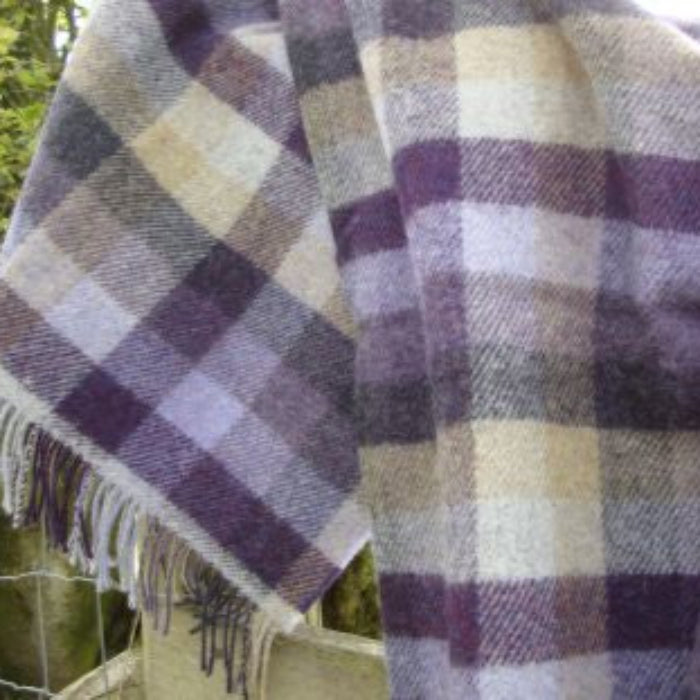 Plaid blanket with lilac, grey and beige colours draped over a surface outdoors.