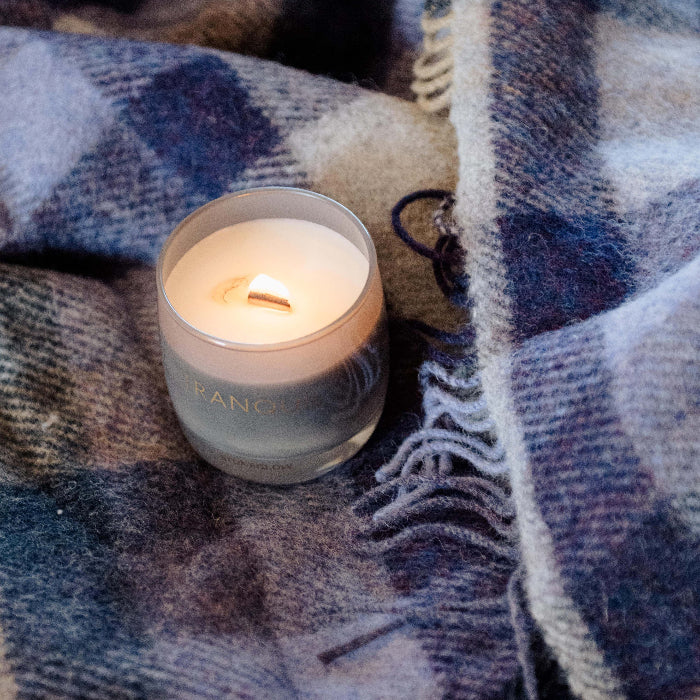 Candle in a glass holder on a plaid wool blanket with colours of lilac, grey and beige