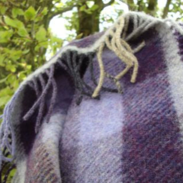 Textured lilac, grey and beige plaid wool blanket with fringe details against a natural background