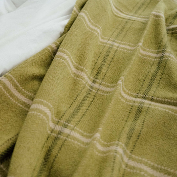 Close up of an emerald green with white stripe plaid throw on a white bed