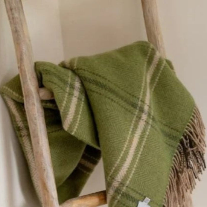 Emerald green plaid throw draped over a wooden ladder against a neutral wall