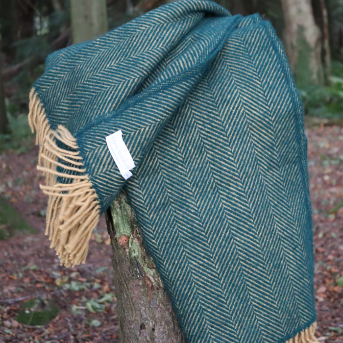 Emerald and mustard herringbone style wool blanket, with a Solway Blankets label, draped over a tree stump in a forest setting.