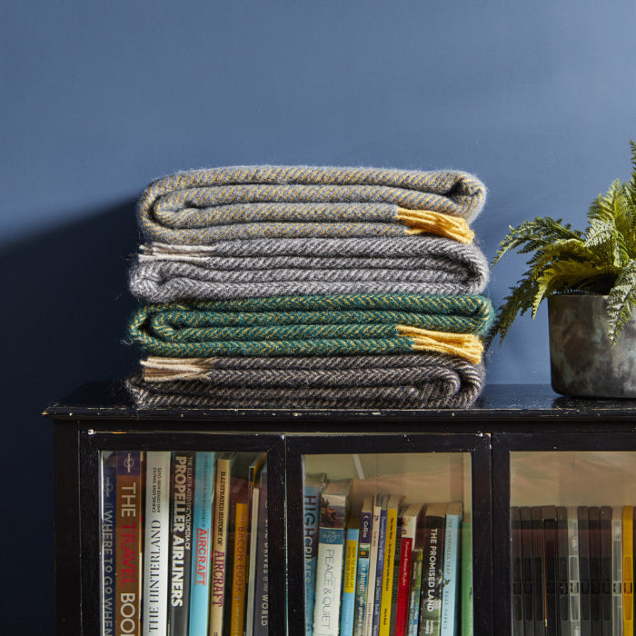 Stack of three folded herringbone style wool blankets on a bookshelf with a blue wall background