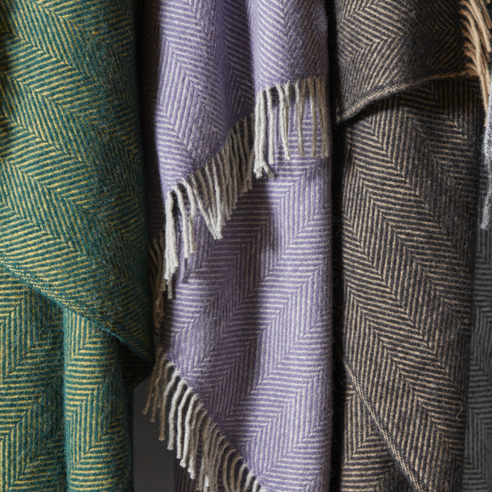 Close up of three herringbone patterned wool blankets with fringes, hanging beside each other
