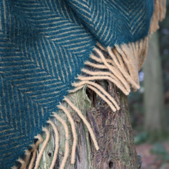 Emerald and mustard herringbone patterned wool blanket with fringe, draped over a tree trunk in a forest setting