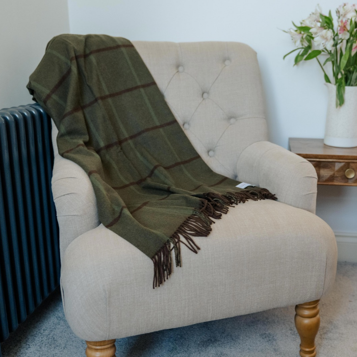 Green and brown Scottish cashmere blanket folded on a cream upholstered armchair