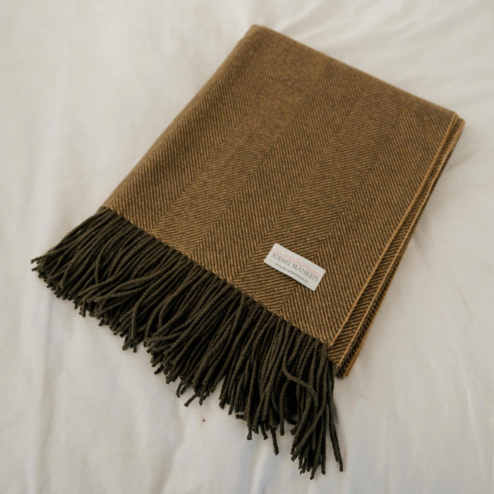 Olive-grey and ochre herringbone lambswool blanket folded across white bedding in a country bedroom