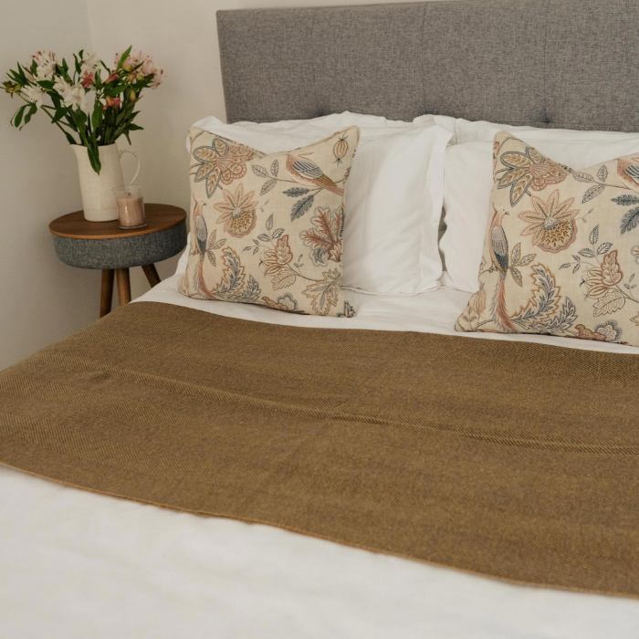 Olive-grey and ochre herringbone lambswool blanket folded across white bedding in a country bedroom