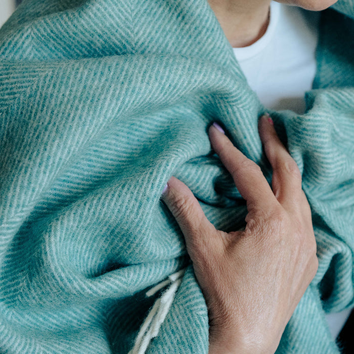 Person wrapped in a cosy eucalyptus herringbone blanket with a Solway Blankets label at a marble surface