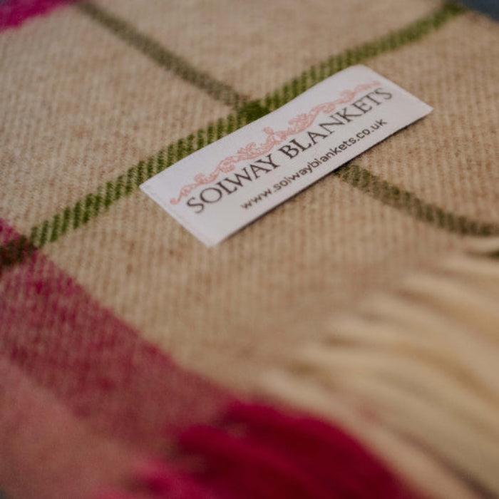 Close-up of a Solway Blankets label on a Falmouth Pink & Ivory Check Shetland Wool Blanket with pink, green, and beige colours.