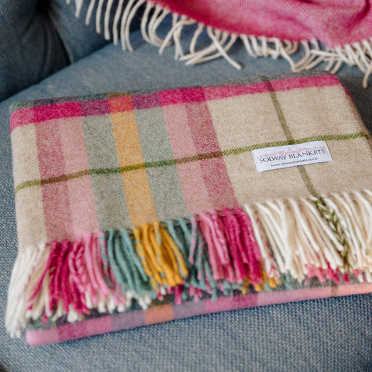 Falmouth Pink & Ivory Check Shetland Wool Plaid blanket with colourful fringes on a blue grey sofa, featuring a Solway Blankets brand label.